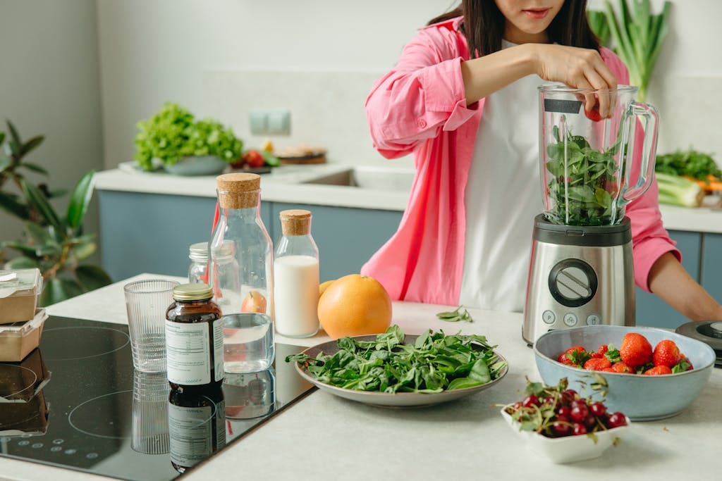 Woman in pink sleeve blending fresh fruits and veggies for a healthy smoothie.