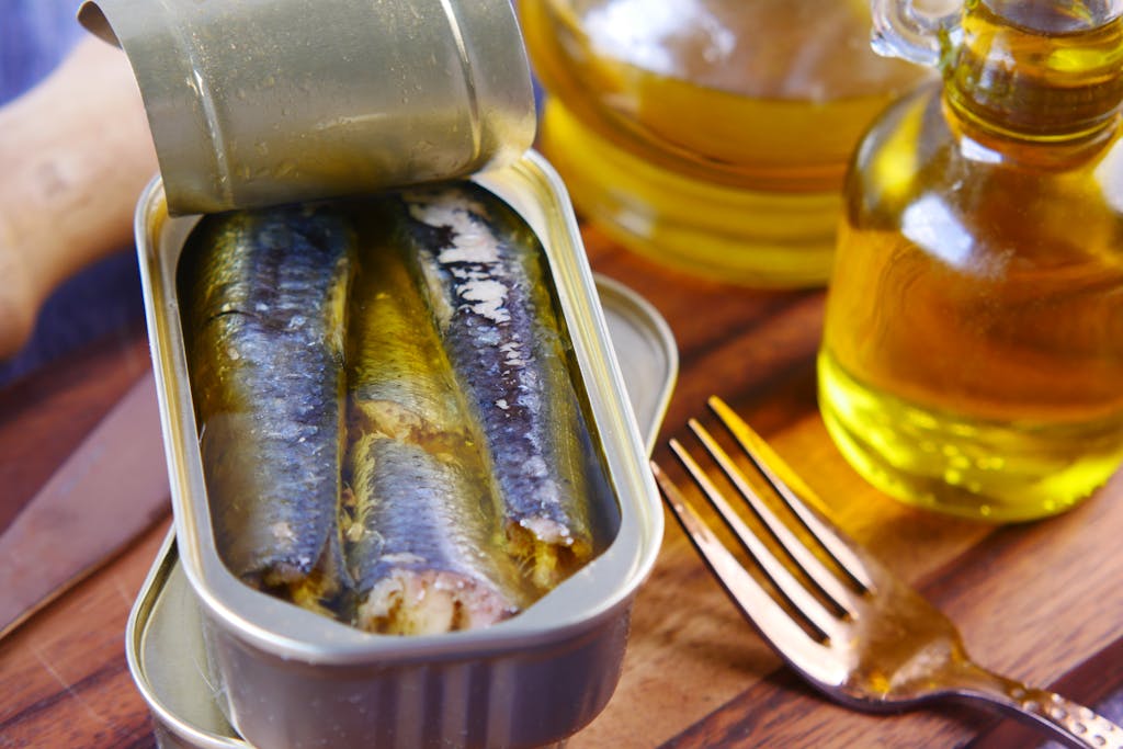 Close-up of canned sardines in olive oil with a fork on a wooden surface.