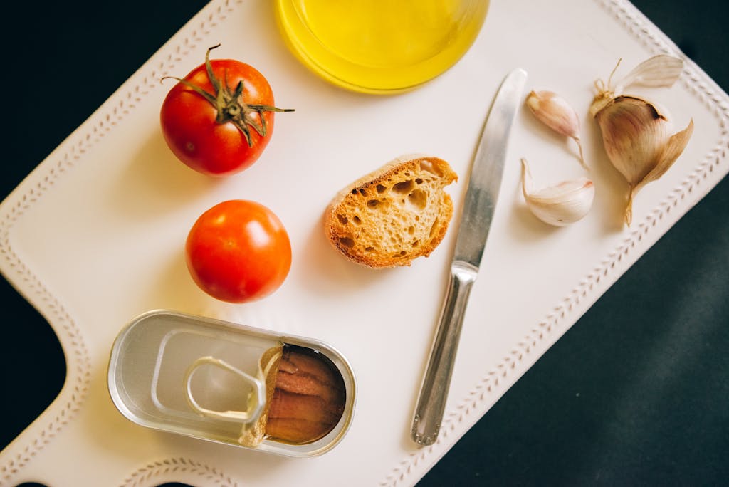 Tomatoes, bread, and sardines arranged for Catalán toast preparation.